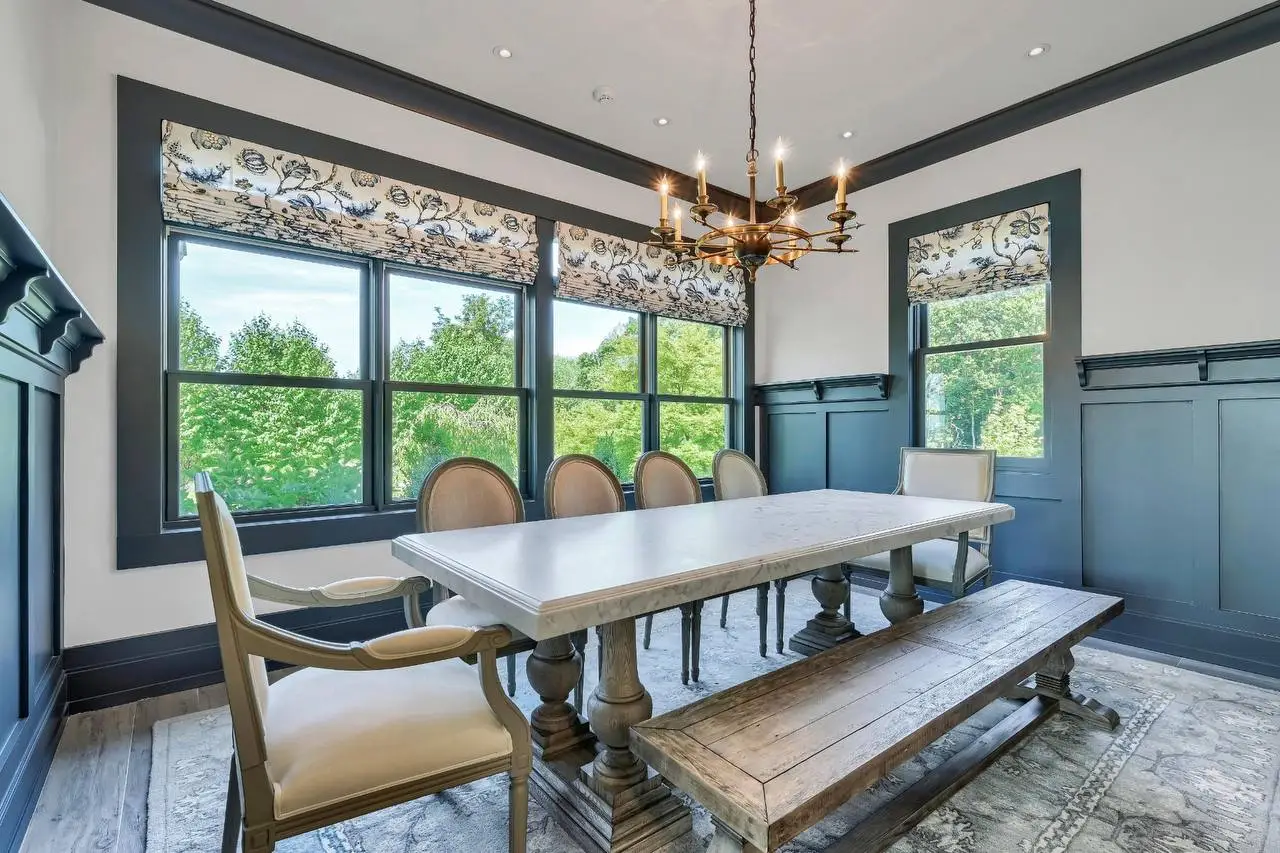 Formal dining room at The Maple Overlook — marble farm table, brass chandelier, navy wainscoting, garden views — private estate upstate New York