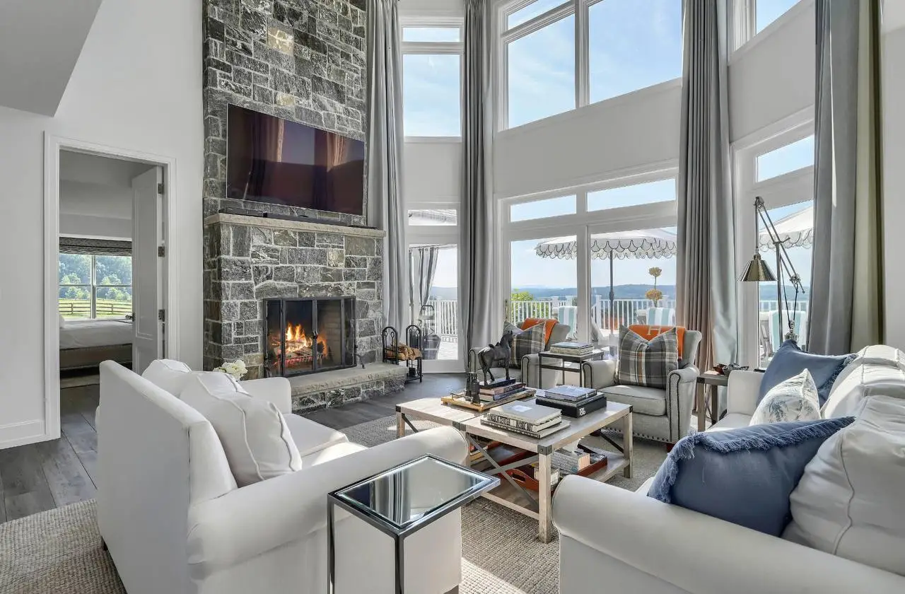 Grand living room at The Maple Overlook with floor-to-ceiling windows, stone fireplace, and Hudson Valley views — private estate upstate New York